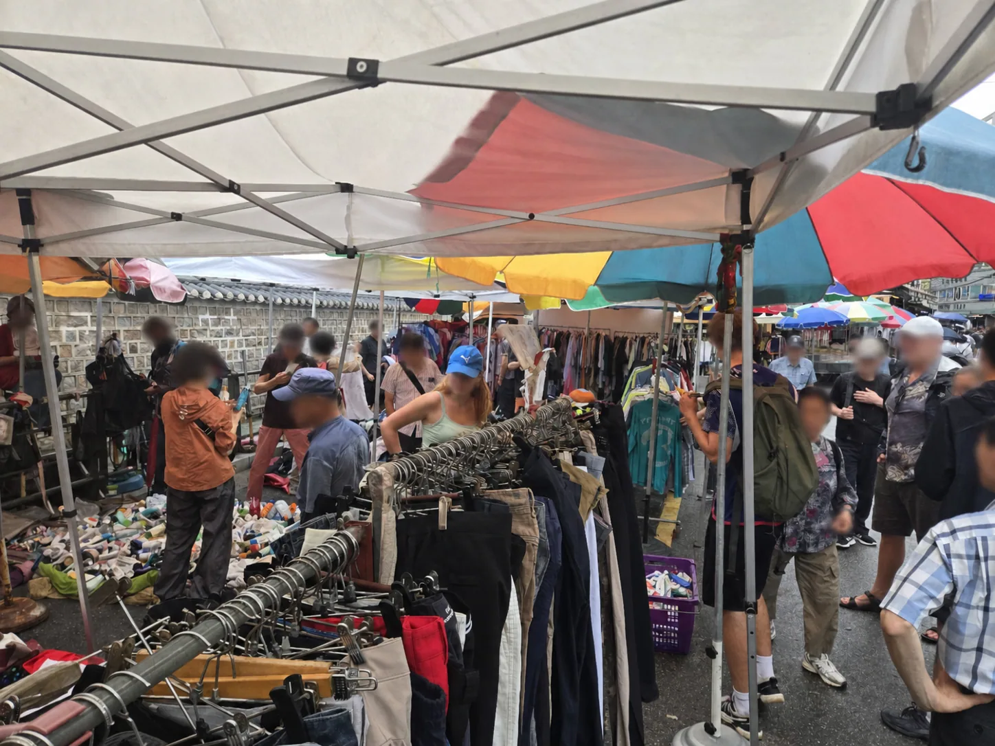 Crowded outdoor clothing stalls under umbrellas at Dongmyo Flea Market