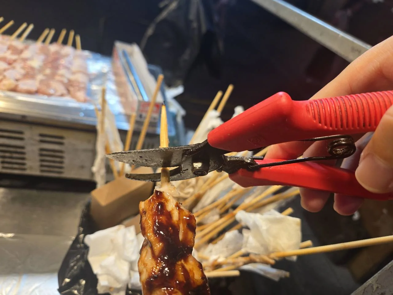 Scissors cutting a wooden chicken skewer while eating dakkochi