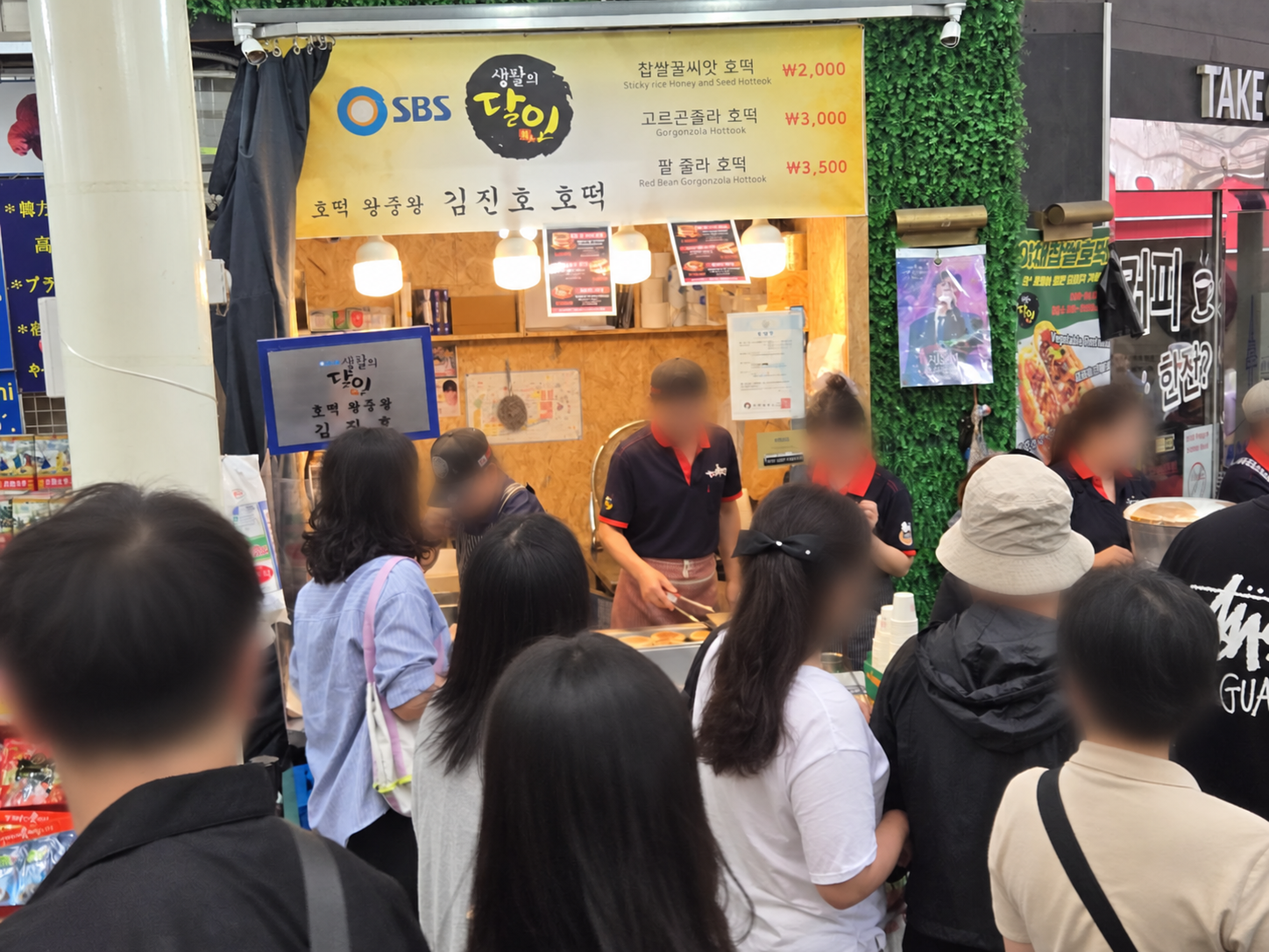 Namsan Kim Jin Ho Hotteok stall with current menu board and queued customers; faces blurred for privacy