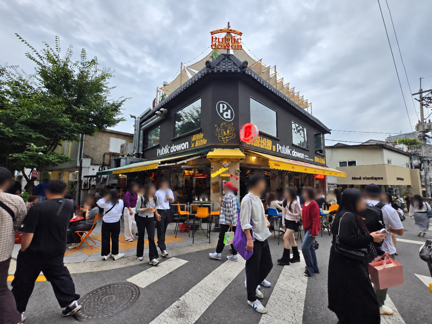 Lively corner venue and pedestrians on Seosulla-gil in Seoul; faces blurred for privacy