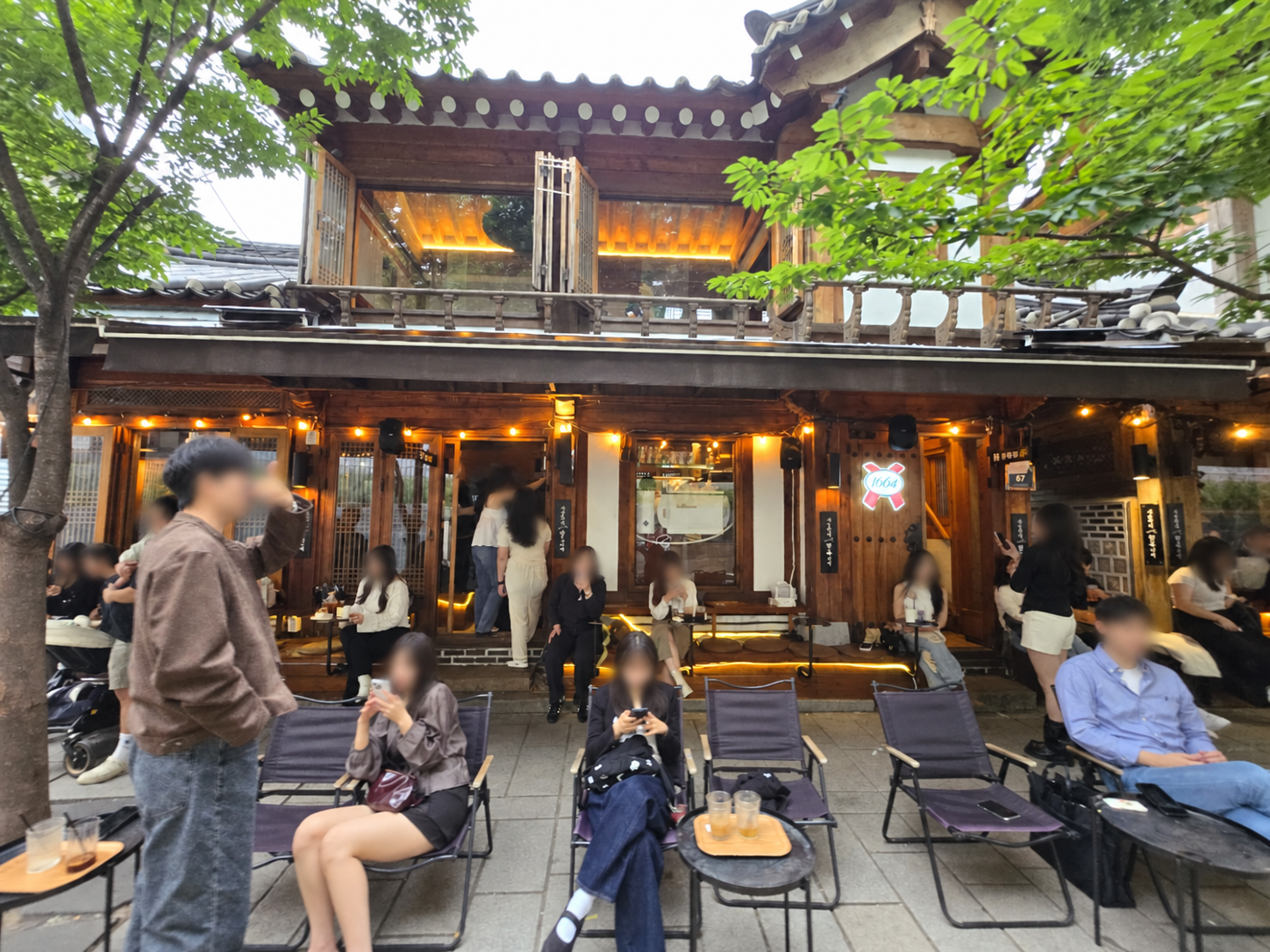 Hanok-style café patio on Seosulla-gil in Seoul at dusk; faces blurred for privacy