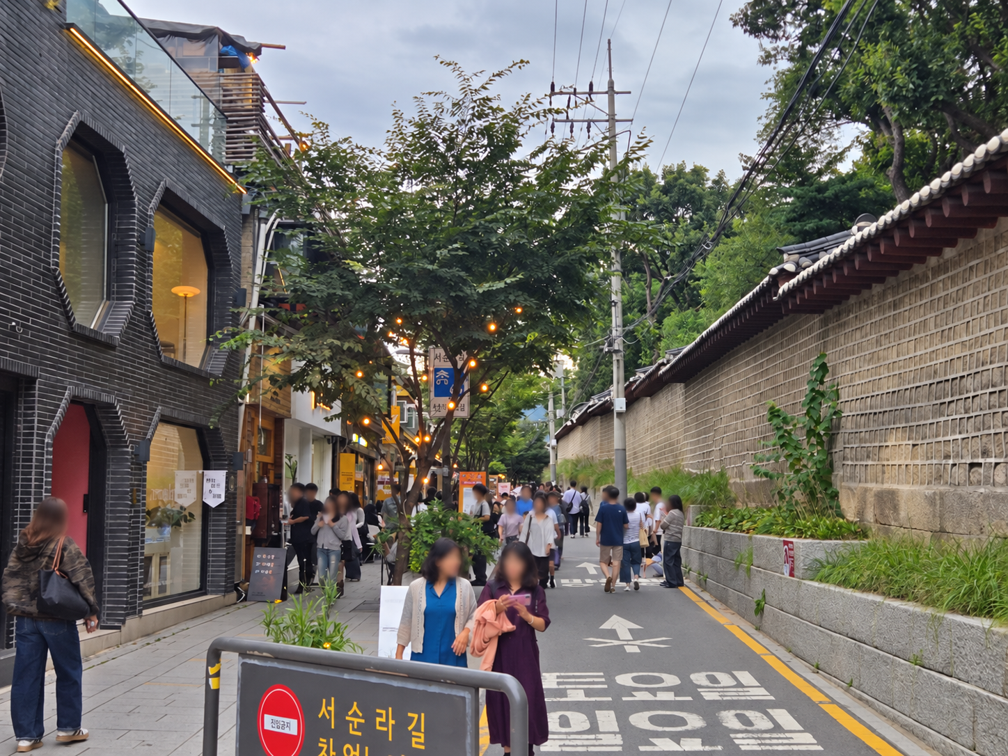 Seosulla-gil street sign beside the historic Jongmyo wall in Seoul; visitor faces blurred for privacy