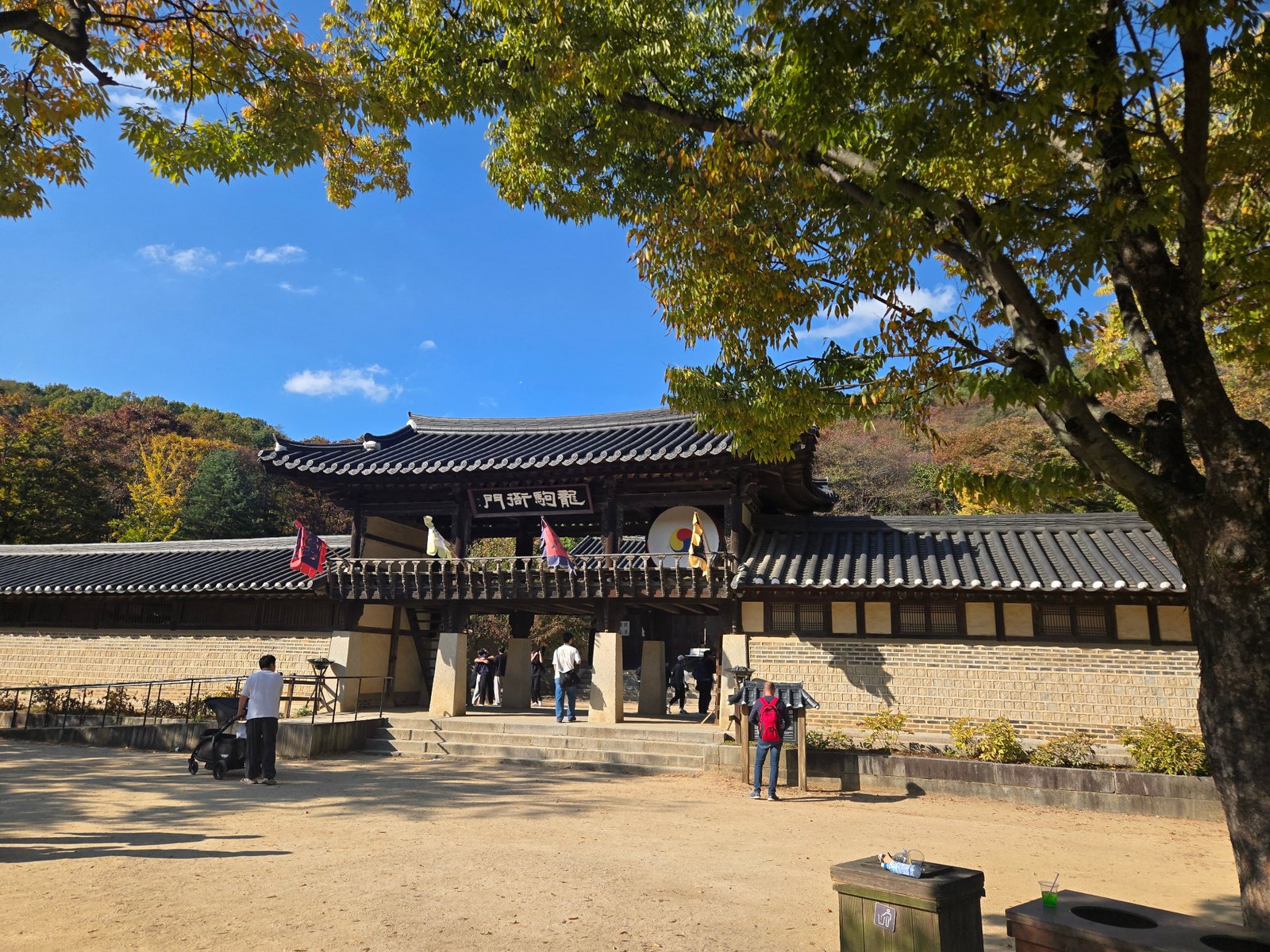 Traditional tiled gate and courtyard framed by trees at Korean Folk Village in Yongin